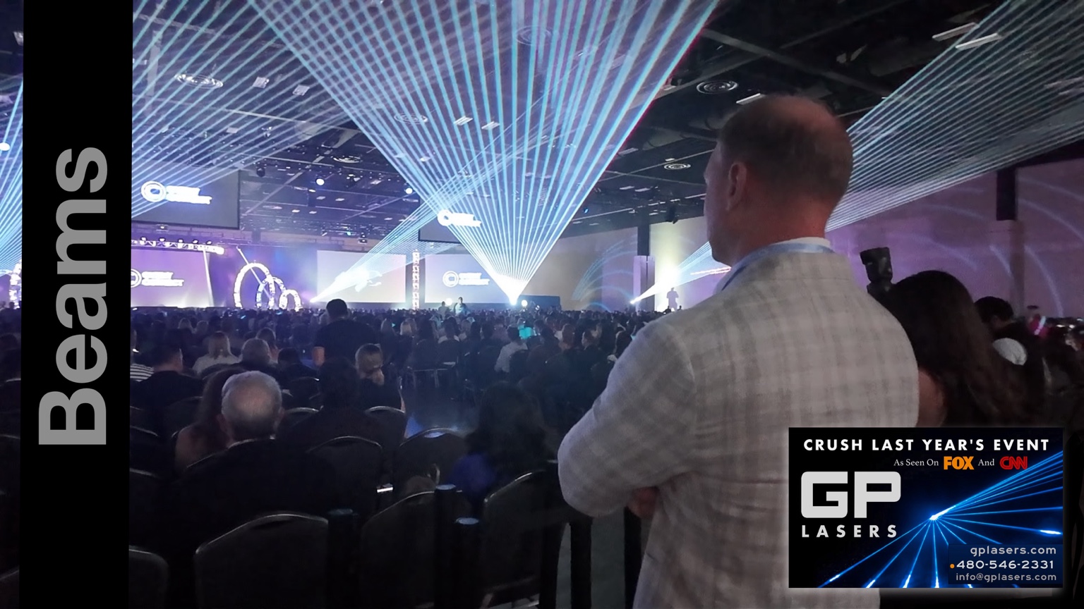 Blue and white laser beams spanning a packed ballroom above seated event guests